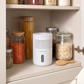 A white Pro Breeze moisture absorber device sits on a kitchen pantry shelf next to glass jars of pasta, oats, and spices.