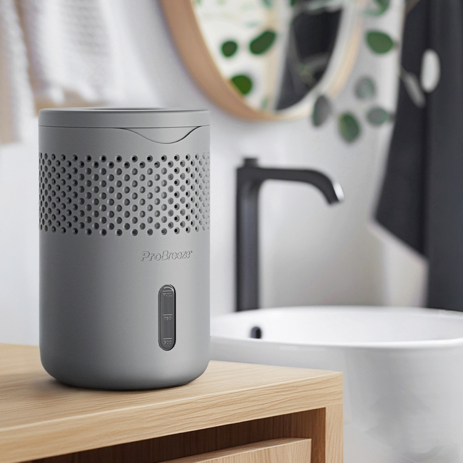 A gray ProBreeze humidifier sits on a light wood bathroom counter with a blurred sink and faucet in the background.